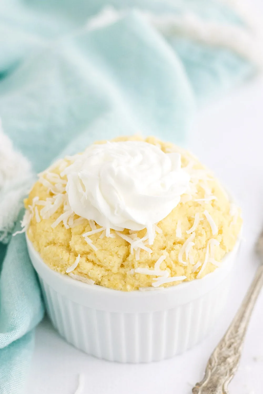 Coconut mug cake topped with shreds and whipped topping in a dish.