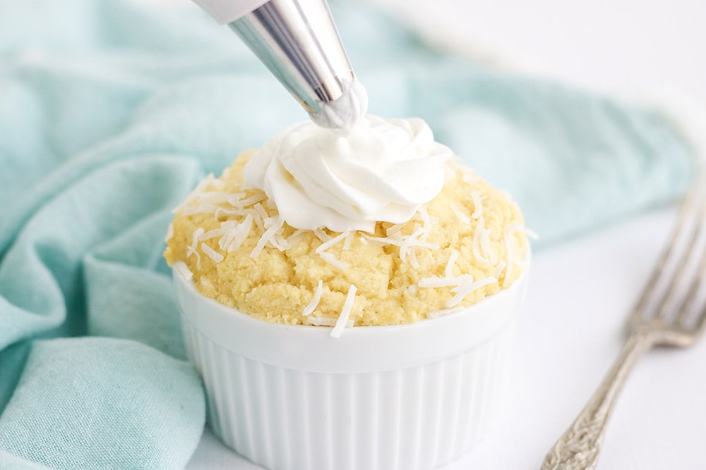 Piping whipped cream onto a yellow cake in a white dish.