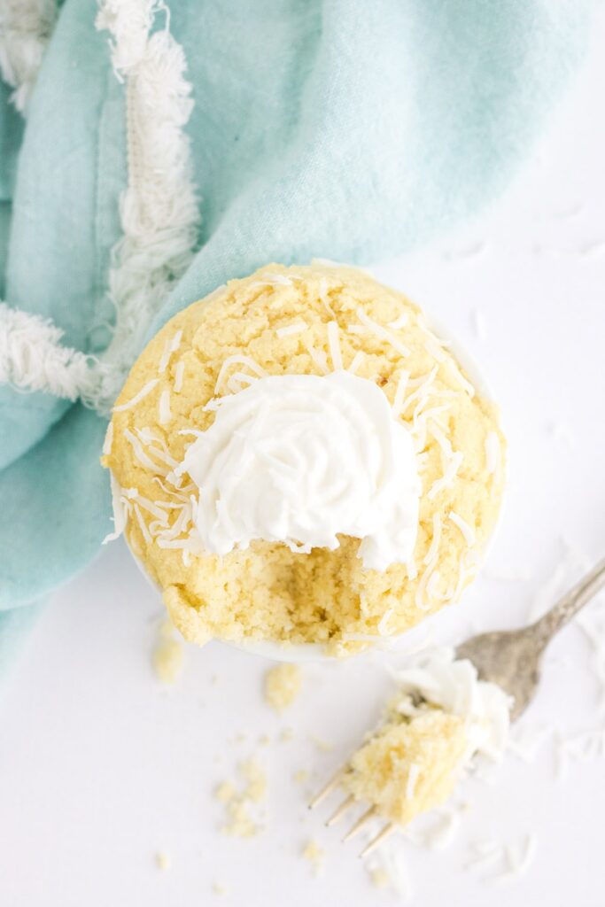 Overhead image of a yellow cake with whipped cream with a fork full of cake missing and sitting next to it.