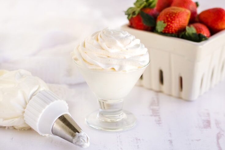 Whipped topping in a glass next to a piping tube and a container of strawberries.