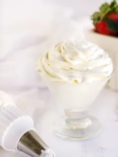 Whipped topping in a glass next to a piping tube and strawberries.