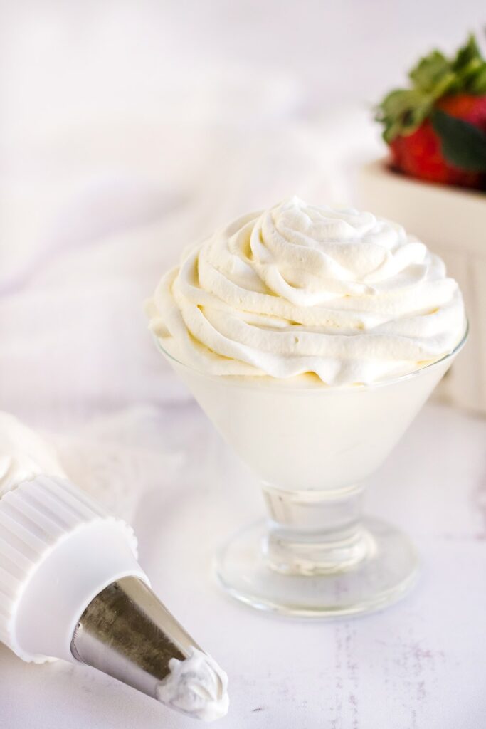 Whipped topping in a glass next to a piping tube and strawberries.