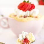 Fork of cake in front of a pink mug with strawberry cake in it.