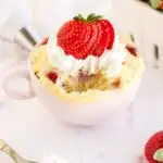 Fork of cake removed from a pink mug full of cake with strawberries.