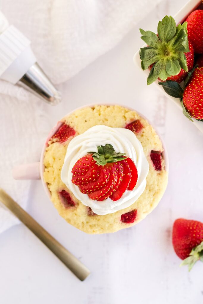 Overhead shot of a strawberry cake in a mug with berries on the table.