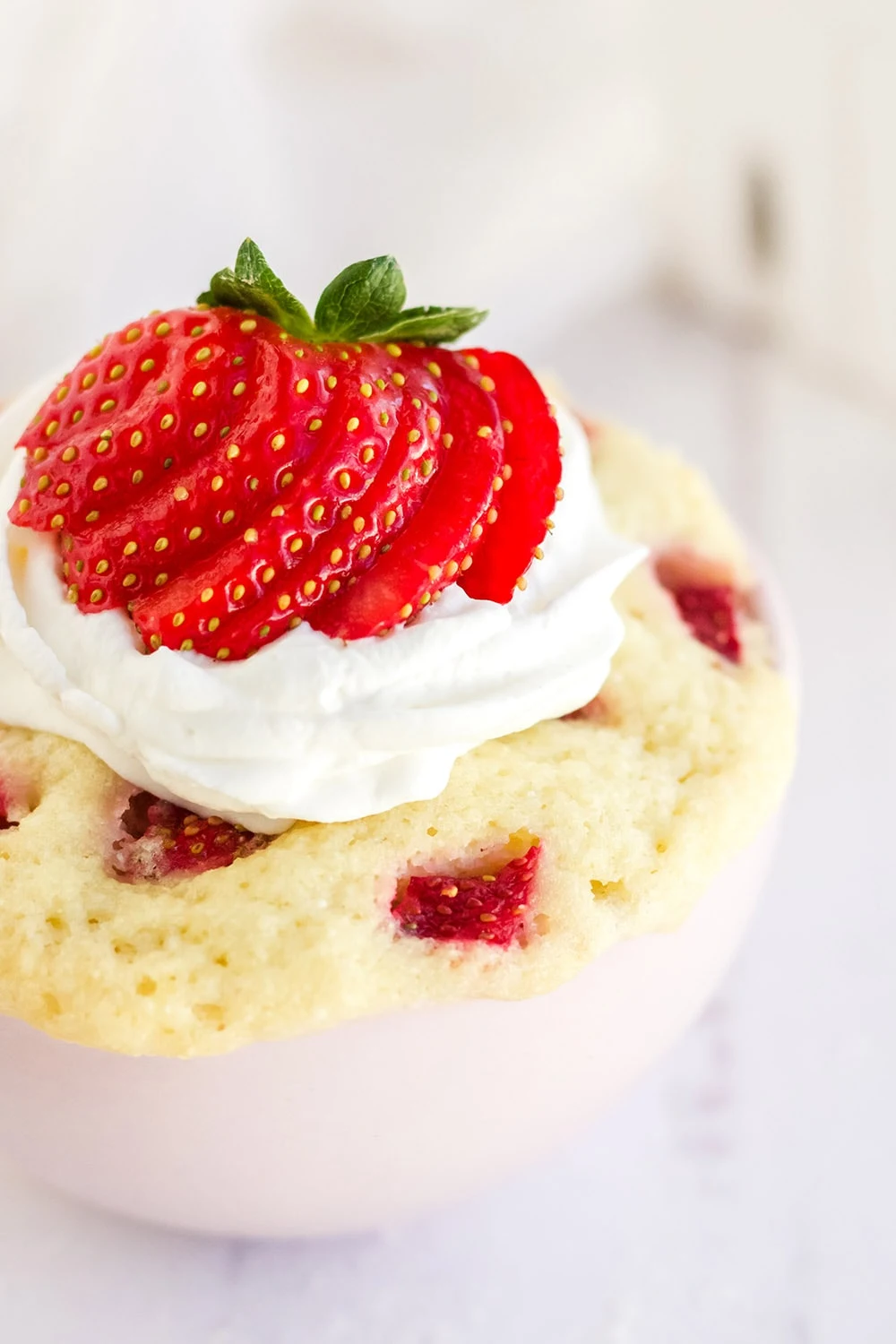 Close shot of a mug cake with sliced strawberries and whipped topping.