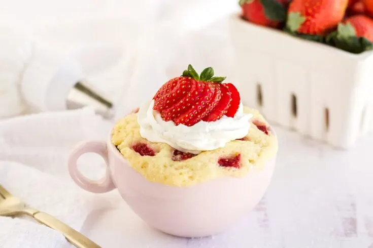Cake with strawberries and whipped cream in a pink mug.